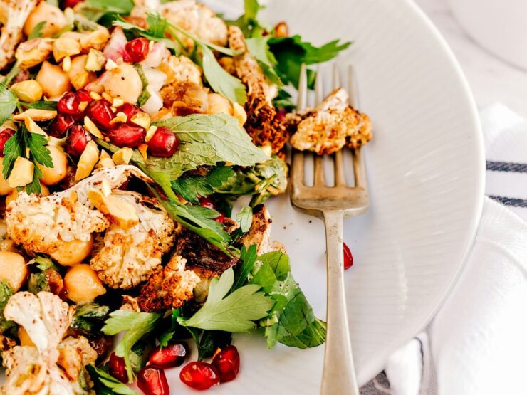 Roasted cauliflower and chickpeas with flat-leaf parsley and pomegranate seeds on a white plate, an antique fork alongside