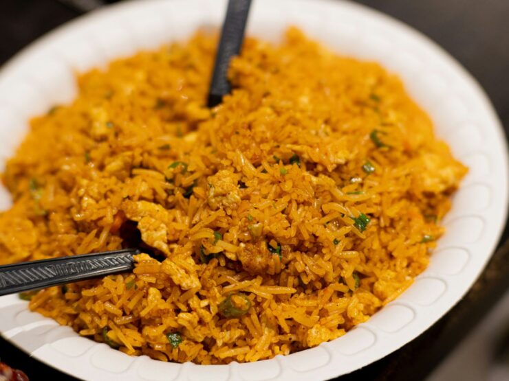 A white bowl of golden egg fried rice flecked with spring onion, two black spoons resting in it