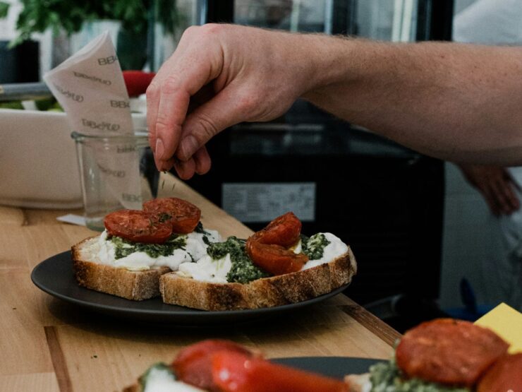 Open sandwiches on a dark plate: toasted sourdough spread with pesto, torn mozzarella and roasted tomato halves