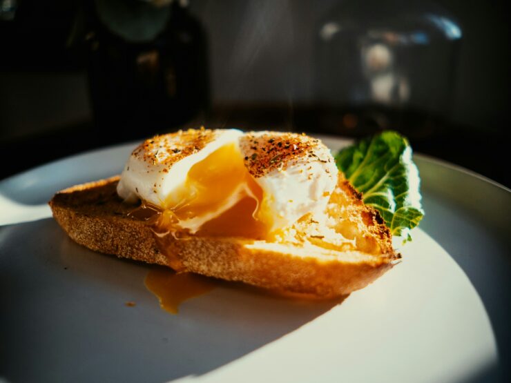 A slice of toast on a white plate topped with a soft egg, the yolk broken and running, steam rising